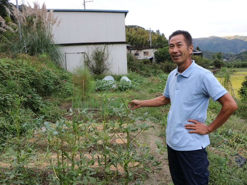 自身の畑の前で笑顔の護さん